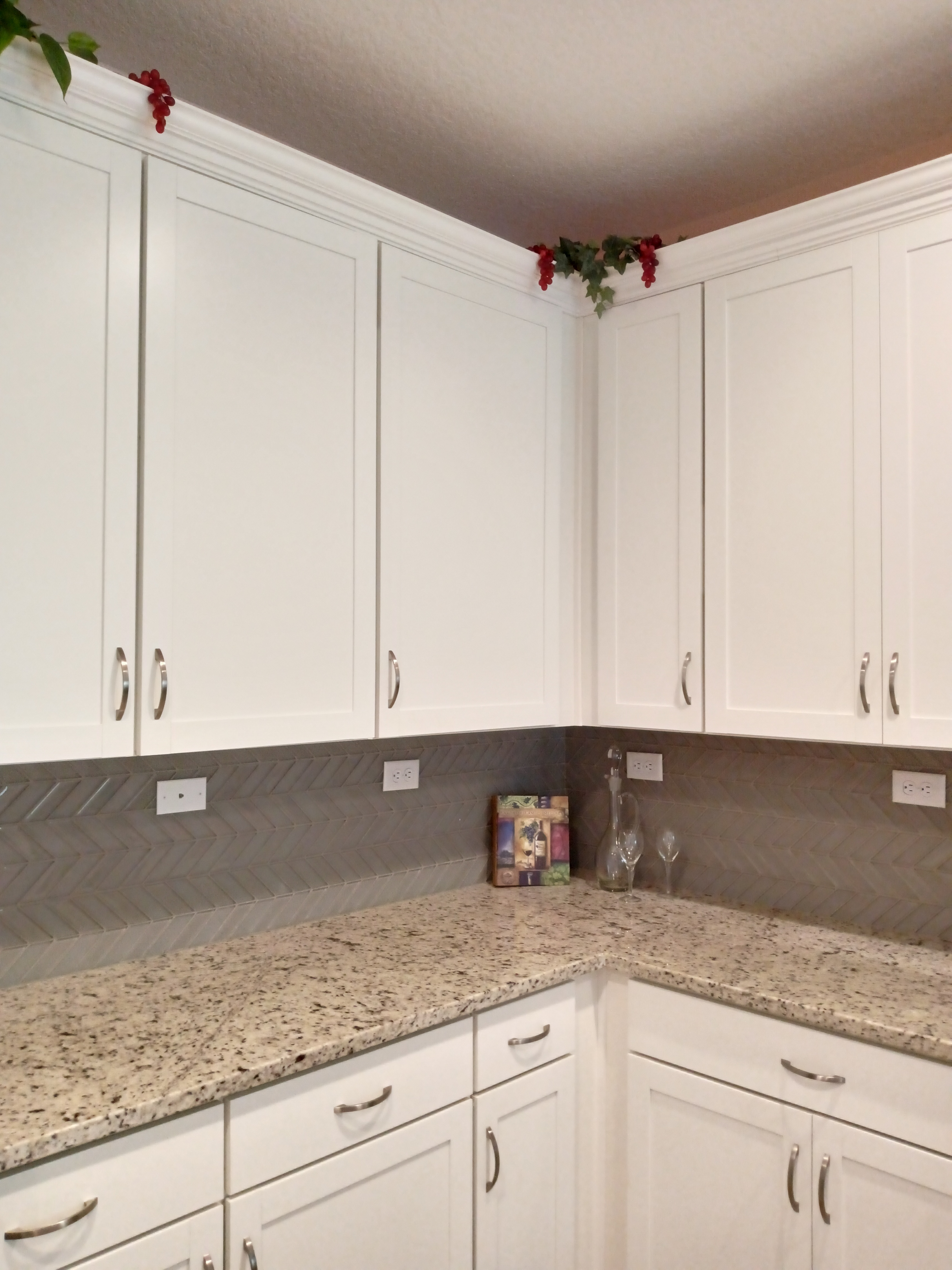 Kitchen with white shaker cabinets, granite countertops, and herringbone tile backsplash